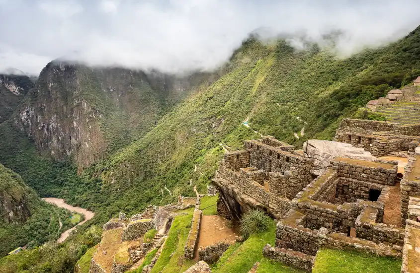 Vista ampla de Machu Picchu, com suas estruturas de pedra e montanhas verdes envoltas por nuvens baixas.