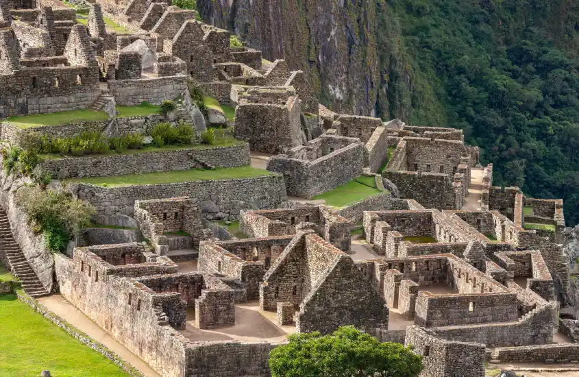 Construções de pedra em Machu Picchu, formando uma complexa organização arquitetônica com terraços verdes, destacando a genialidade da engenharia inca.