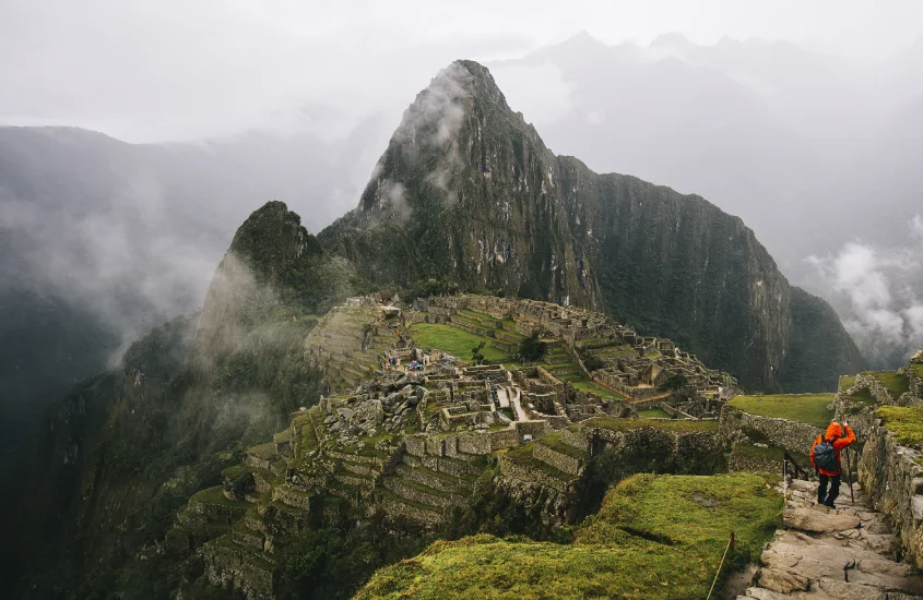 Vista ampla de Machu Picchu com Huayna Picchu ao fundo, envolta por neblina, criando um cenário dramático e inesquecível.