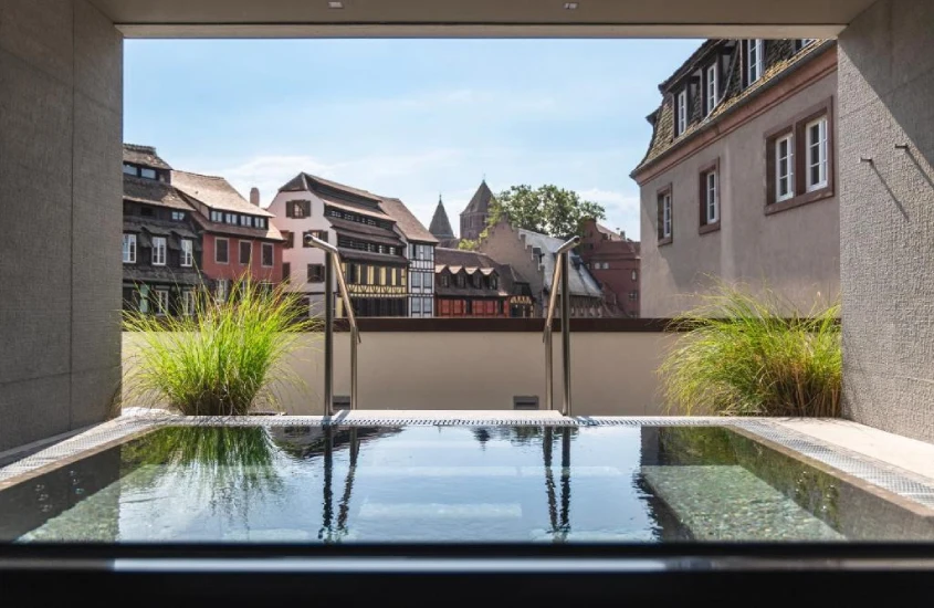 Piscina com vista para construções históricas em estilo enxaimel, emoldurada por vegetação moderna.