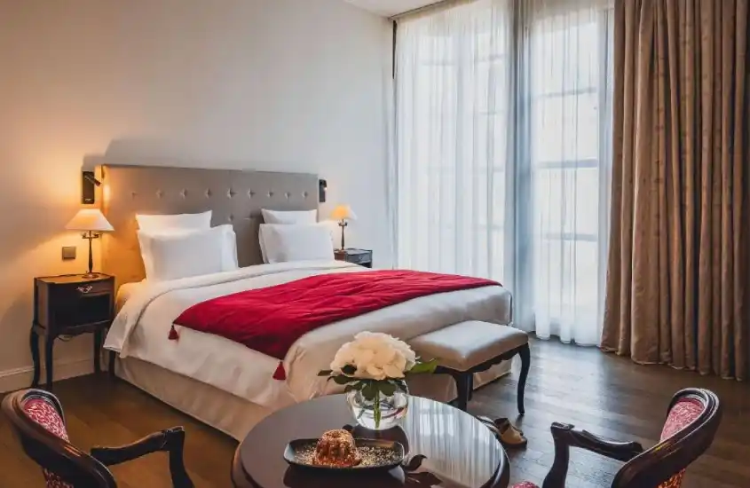 Quarto de hotel em Estrasburgo com cama de casal, detalhes em vermelho e preto, e uma mesa decorada com flores.