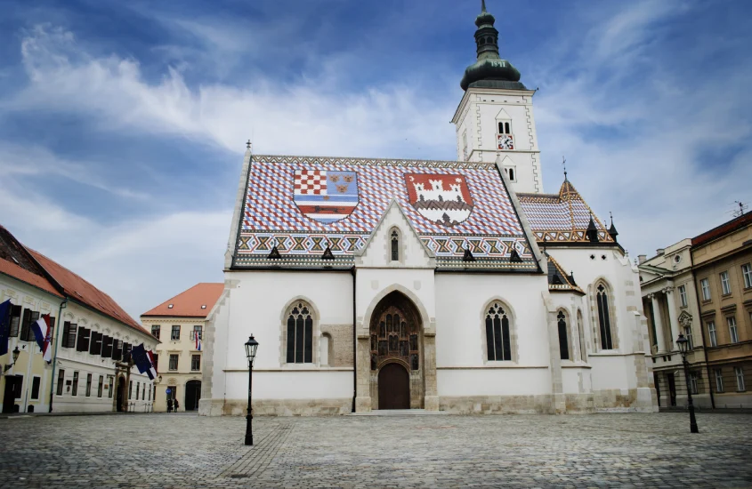 Fachada da Igreja de São Marcos, com seu icônico telhado colorido e detalhes arquitetônicos históricos na Cidade Alta de Zagreb.