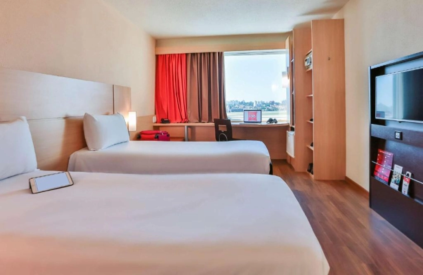 Quarto de hotel com camas, área de trabalho e janela com vista da cidade