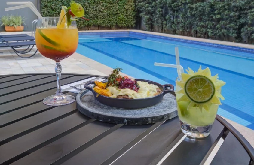 Área de lazer do hotel com piscina e mesa com petiscos e drinks