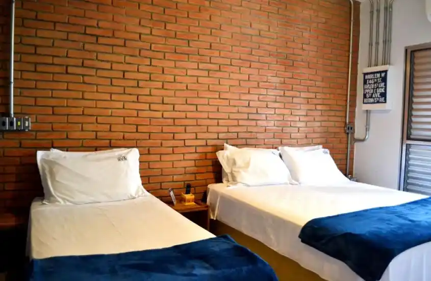 Quarto com cama de casal e cama de solteiro com cobertas azuis e parede de tijolinhos