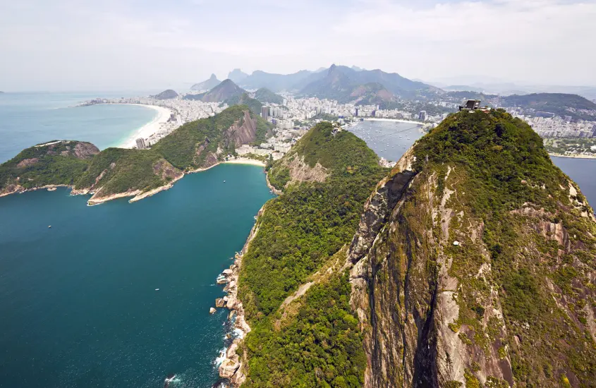 Vista aérea do Rio de Janeiro, destacando as praias de Copacabana e Ipanema, rodeadas por montanhas e vegetação.