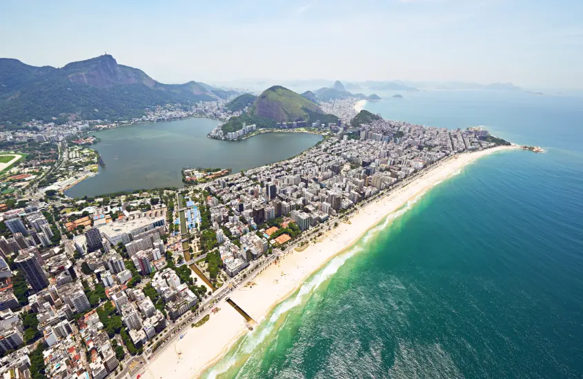 Vista aérea do bairro de Ipanema, mostrando a Lagoa Rodrigo de Freitas cercada pela urbanização e a praia com águas claras.