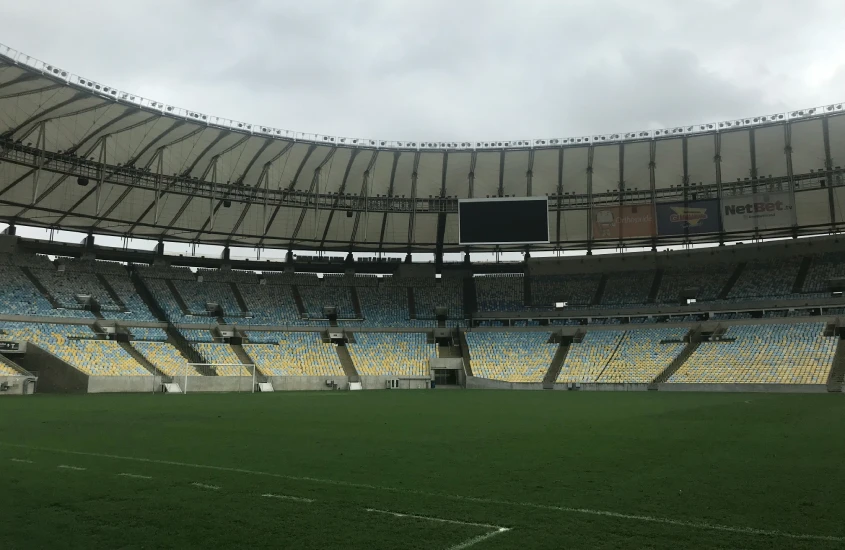 Interior do estádio do Maracanã com gramado central e arquibancadas vazias em um dia nublado.