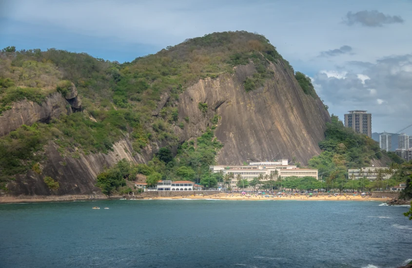 Praia Vermelha, no Rio de Janeiro, com a imponente encosta do Morro da Urca ao fundo e prédios próximos à areia.