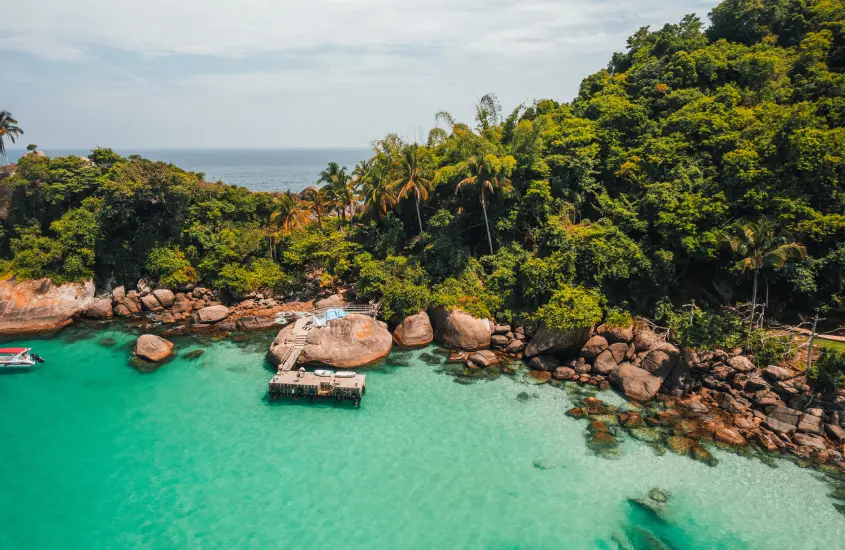 Vista aérea de uma enseada em Ilha Grande, com águas cristalinas e vegetação exuberante ao redor.