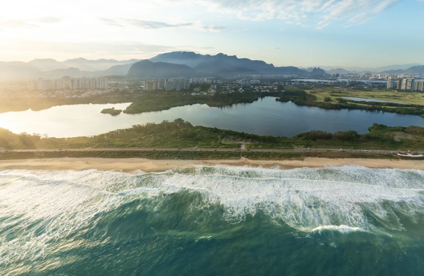 Vista da Barra da Tijuca, com praias extensas, lagoas e montanhas ao fundo, ao amanhecer.