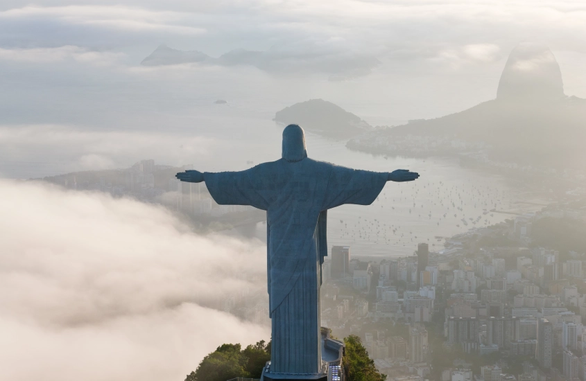 Estátua do Cristo Redentor no topo do Corcovado, envolta por nuvens, com vista panorâmica do Rio de Janeiro.