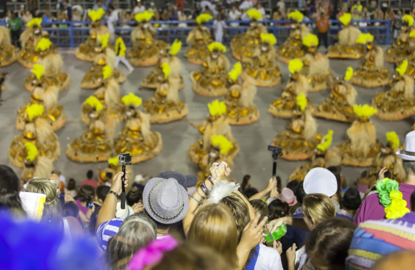 Desfile de Carnaval no Sambódromo, com destaque para fantasias douradas e público vibrante na arquibancada.