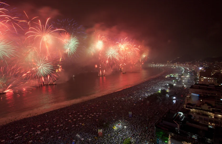 Fogos de artifício na praia de Copacabana durante o Réveillon, iluminando o céu noturno e atraindo multidões.