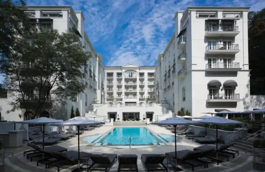 Fachada do Palácio Tangará - an Oetker Collection Hotel, com arquitetura clássica branca, piscina central e espreguiçadeiras ao redor.