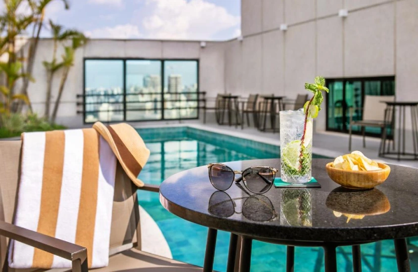 Piscina no terraço do Meliá Jardim Europa, com cadeiras ao pôr do sol e vista da cidade.