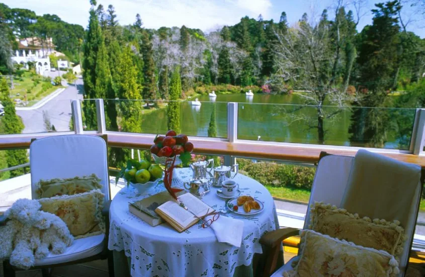 Varanda com mesa decorada para café da manhã, vista para um lago rodeado por árvores.