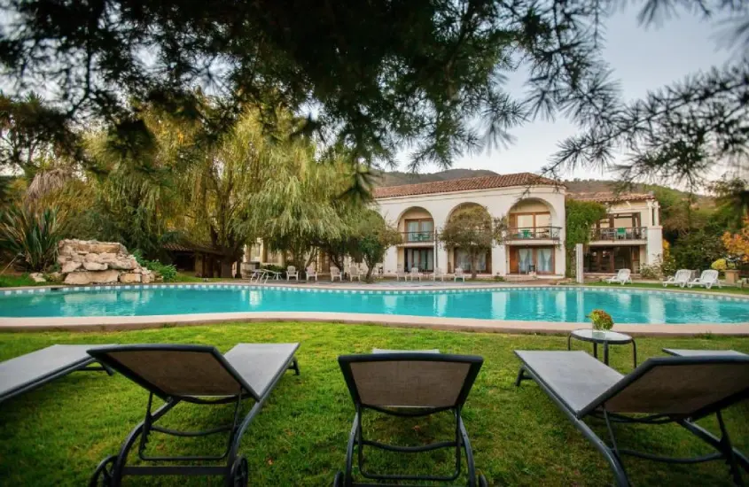 Piscina externa em jardim com mansão ao fundo.