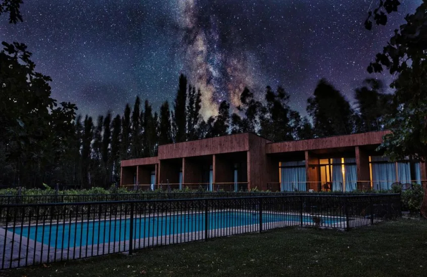 Ambiente noturno, com construção moderna cercada por vinhedos e um céu repleto de estrelas em destaque.