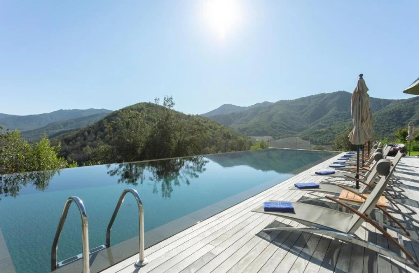 Piscina de borda infinita com vista panorâmica para colinas verdes e céu azul brilhante.