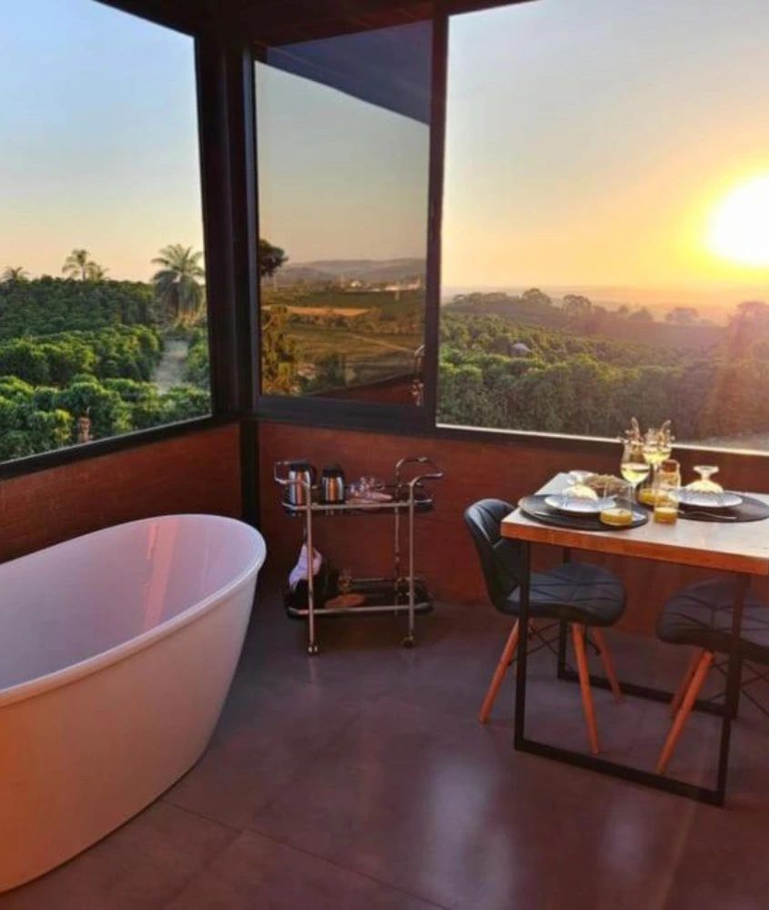 Banheira de design elegante em uma varanda com vista para plantações e pôr do sol, ao lado de uma mesa de jantar posta.