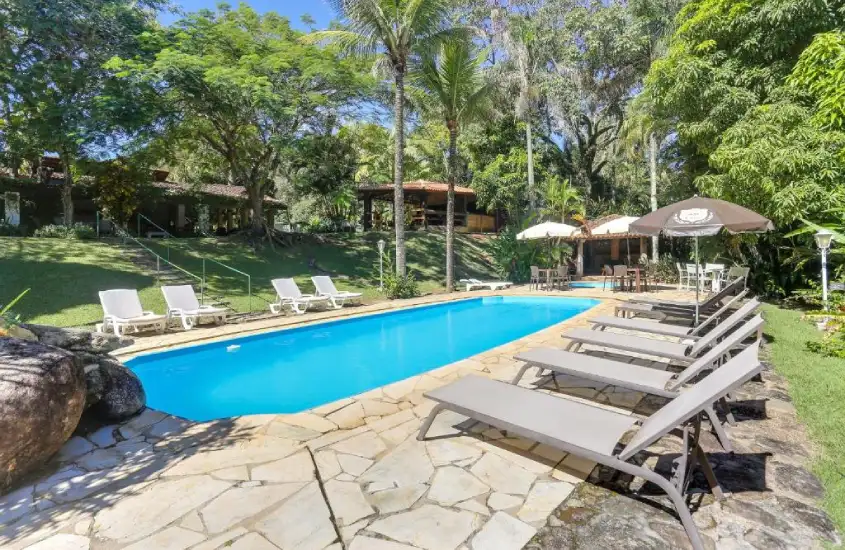 Piscina com espreguiçadeiras em um ambiente arborizado, com sombra de árvores e área de convivência.