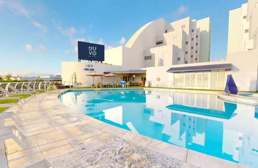 Piscina ampla de hotel com borda infinita e espreguiçadeiras, acompanhada de um prédio moderno e design contemporâneo.