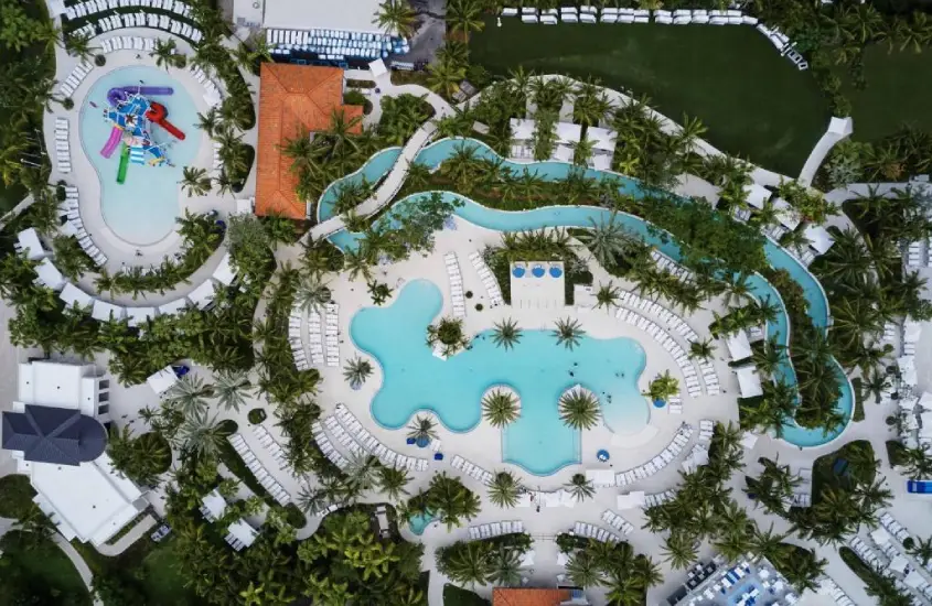 Vista aérea de um resort com várias piscinas, área infantil, palmeiras e um layout espaçoso para lazer.