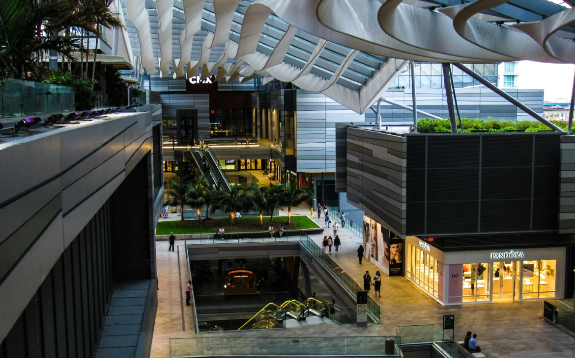 Um shopping center moderno com arquitetura aberta, repleto de lojas de marcas como Pandora e CMA.