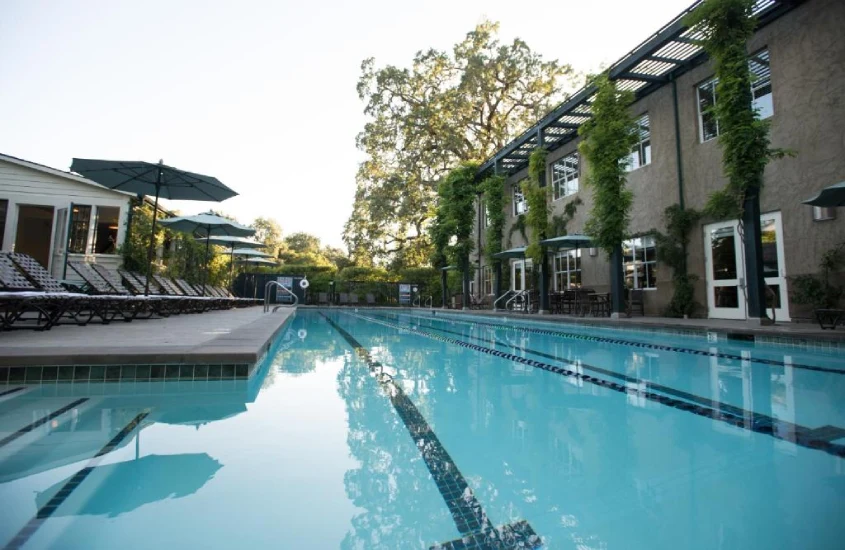 Piscina comprida rodeada por guarda-sóis, espreguiçadeiras e vegetação exuberante.