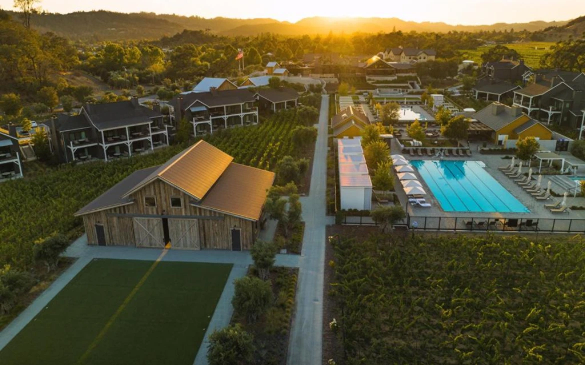 Complexo de hospedagem de luxo em meio a vinhedos, com piscina ampla e paisagem ao pôr do sol.