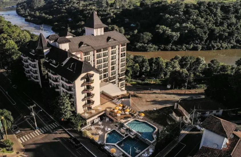 Vista aérea de hotel com piscinas, guarda-sóis, árvores ao redor e lago do lado