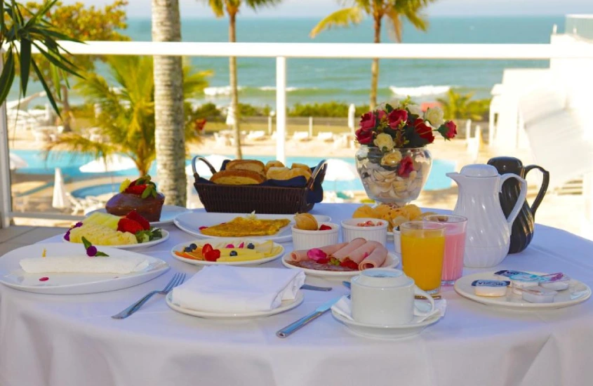 Em um dia de sol, mesa posta de café da manhã com paisagem do mar e da área de lazer com piscina