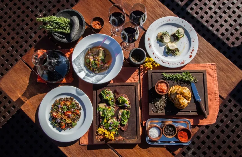 Mesa posta com carne, vegetais, plantas decorativas, temperos pães e vinhos