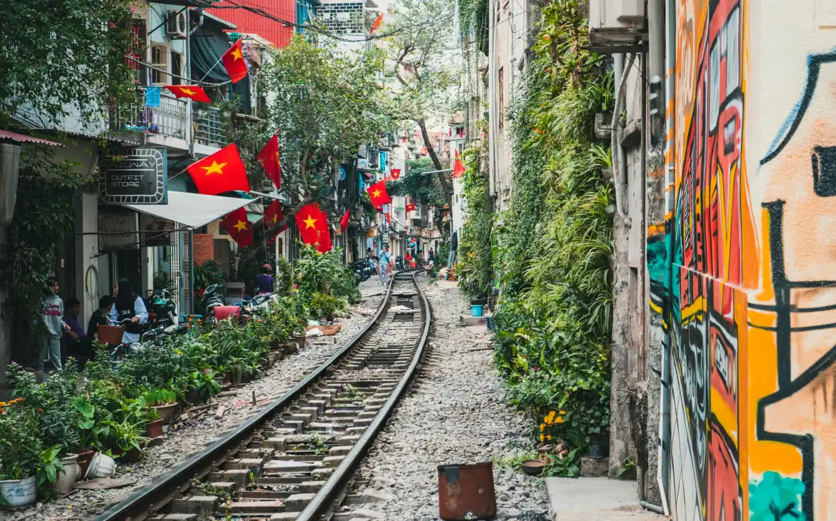 Trilho de trem com construções ao redor, plantas e bandeiras do Vietnã