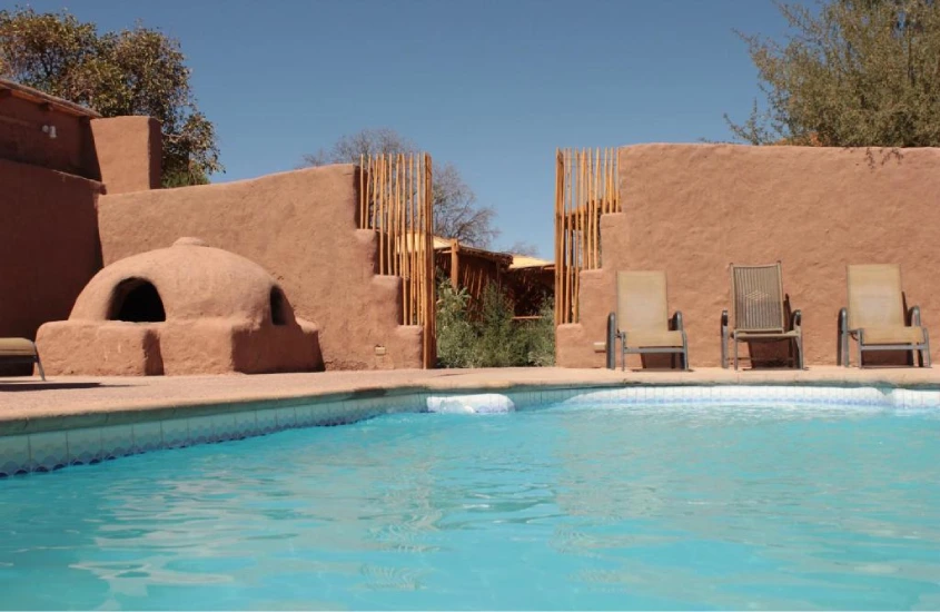 Em um dia de sol, área de piscina com espreguiçadeiras e estrururas de argila