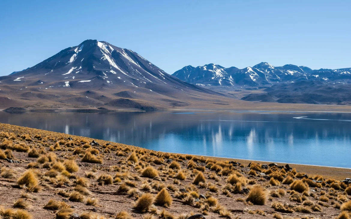 Em um dia de sol, paisagem do deserto do Atacama com oásis no meio, areia e montanhas ao redor