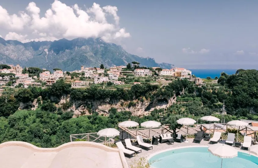 Em um dia de sol,visão aérea de hotel com piscina, mesas, cadeiras, guarda-sóis, espreguiçadeiras e cidade no fundo