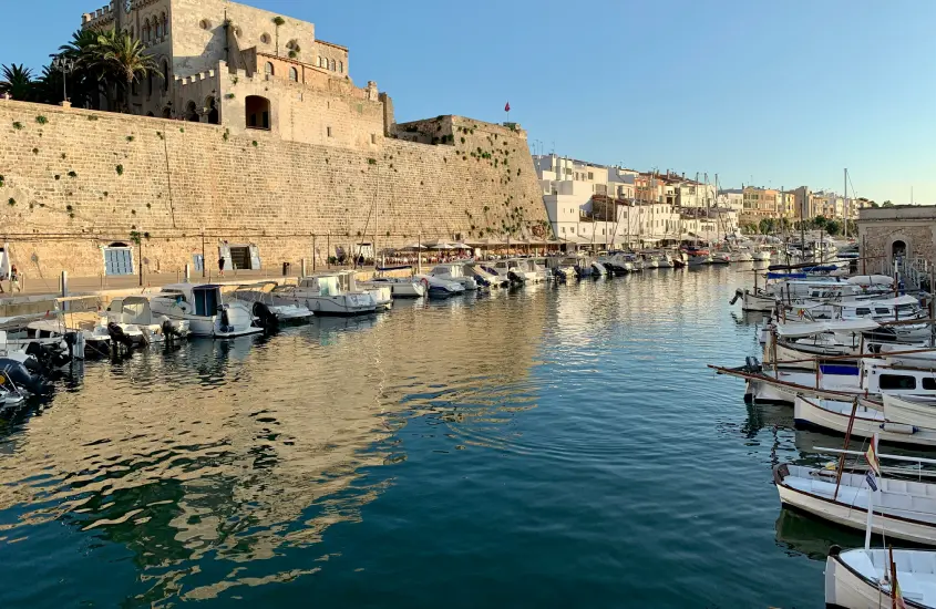 Em um dia de sol, canal com construções antigas do lado e barcos aportados ao redor