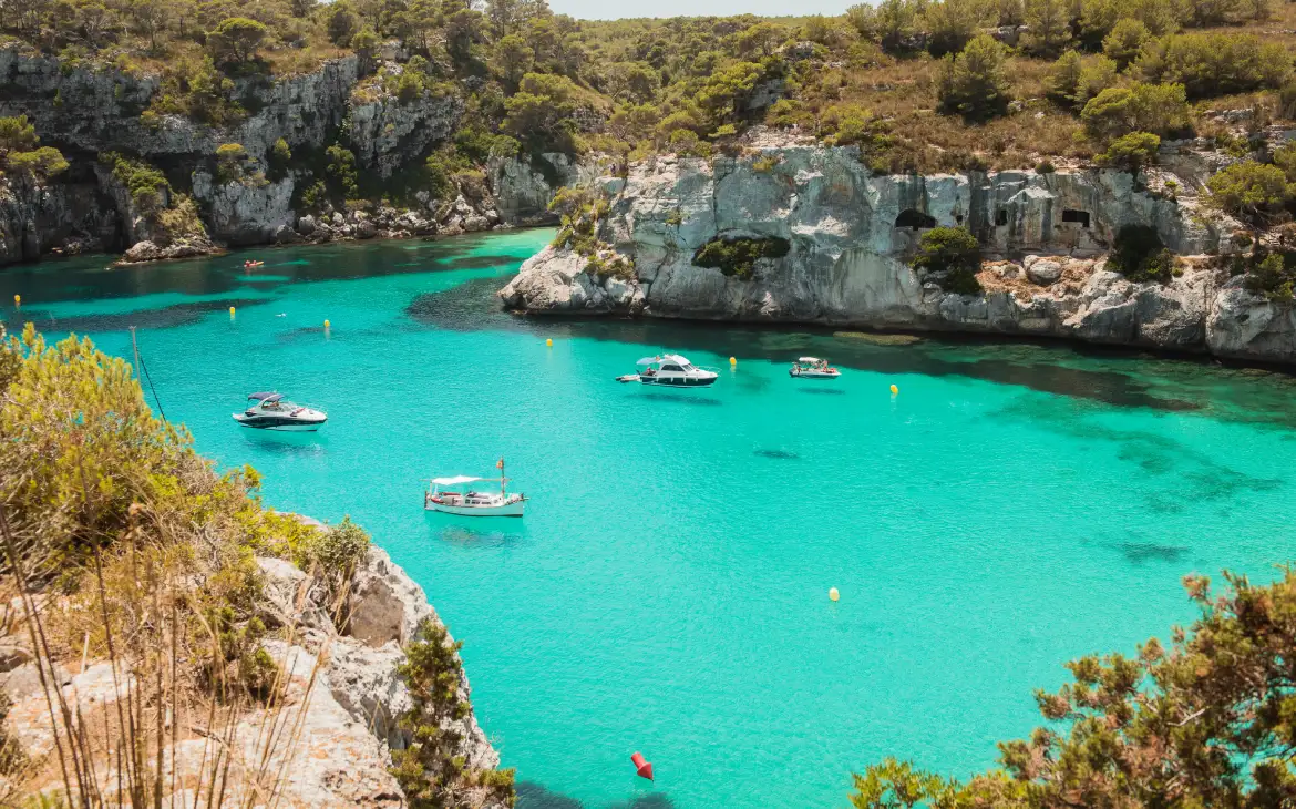 Em um dia ensolarado, visão aérea da ilha com paredões de pedra ao redor, árvores e barcos no mar