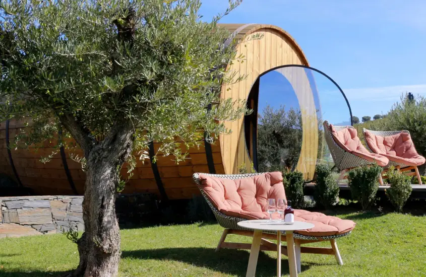 Em um dia ensolarado, cabanas de barril com cadeiras de madeira e mesa relaxantes, e área verde ao redor