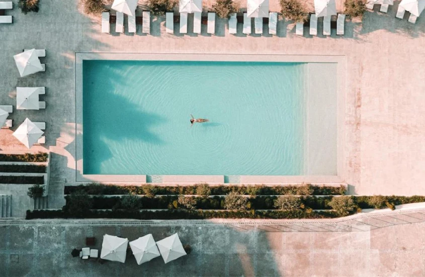 Área de piscina de hotel com espreguiçadeiras, guarda-sóis e plantas ao redor