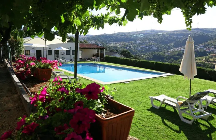 Área de lazer de hotel com piscina, espreguiçadeiras, parreiras de uva, paisagem do rio do lado e flores decorativas