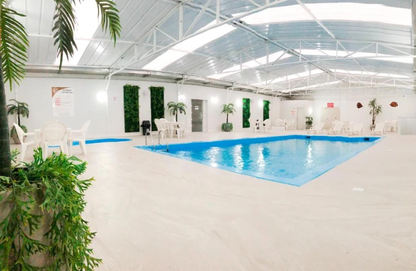 Piscina coberta de hotel com mesas, cadeiras, espreguiçadeiras e plantas decorativas