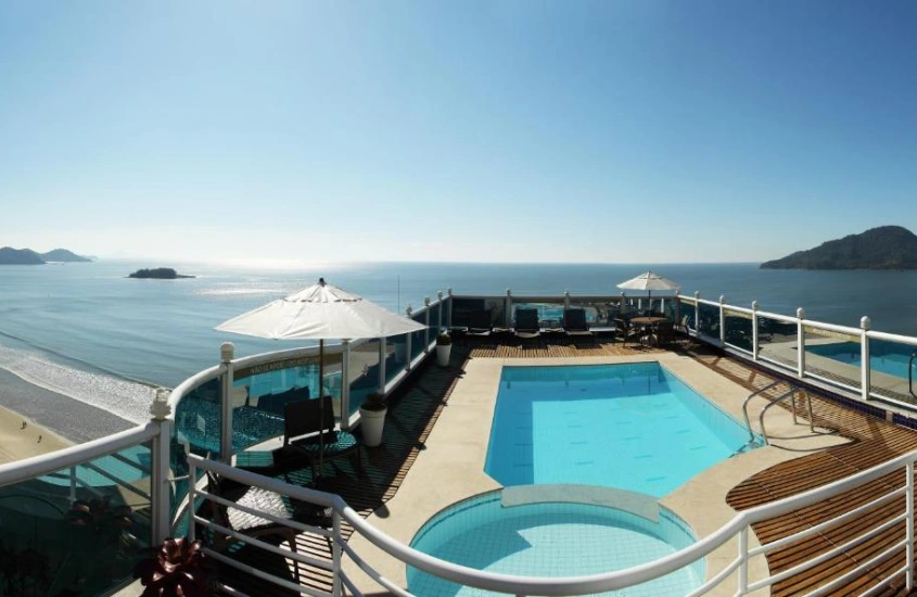 Em um dia de sol, piscina na cobertura de hotel com espreguiçadeiras, guarda-sóis e praia na frente