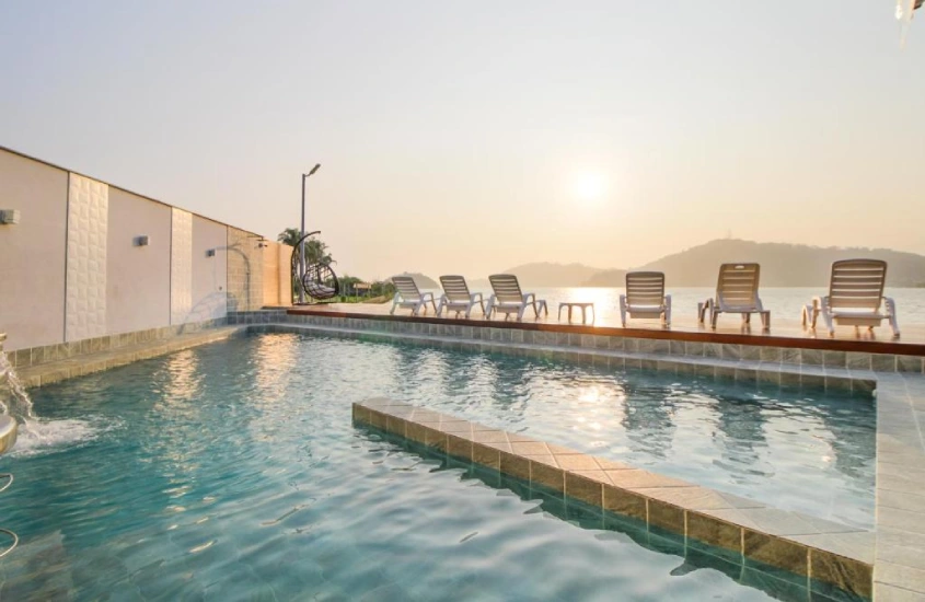 Em um dia de sol, área de piscina de hotel com espreguiçadeiras, piscina e mar na frente