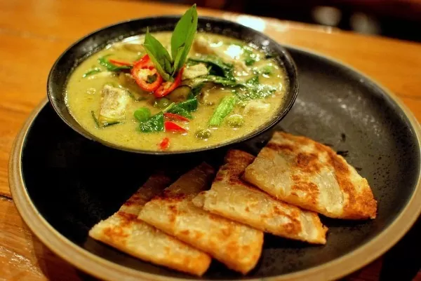 Kaeng Khiao wan um curry verde doce da culinária tailandesa, servido em tigela preta, em cima de mesa de madeira