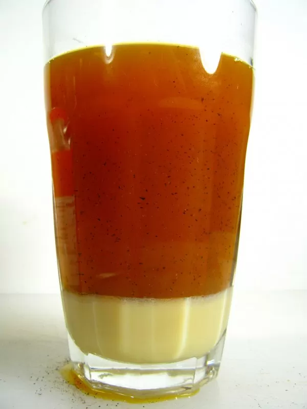 Copo de vidro com leite e chá misturado com flor de laranjeira, em cima de mesa branca