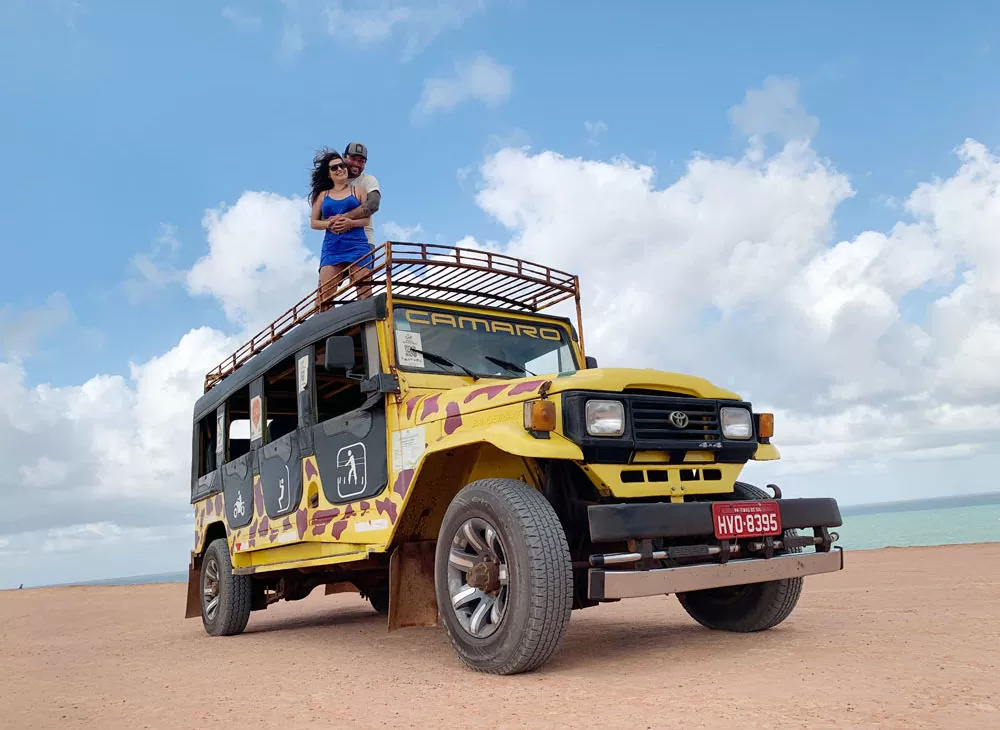 casal viajando o mundo Vagner Alcantelado e Babi Rocha abraçados em cima de jeep amarelo, durante um dia de passeios em pipa