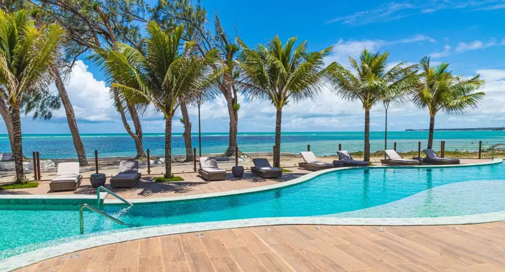 piscina cercada de coqueiros com vista para o mar em área de lazer de Oceana Atlântico Hotel
